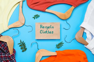 Different clothes with recycling label and hangers on light blue background, flat lay