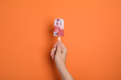 Woman holding berry popsicle on orange background, closeup