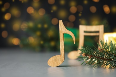 Wooden music note and fir branches on light grey table against blurred Christmas lights