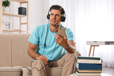 Man with mobile phone listening to audiobook on sofa indoors
