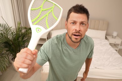 Photo of Man with electric fly swatter in bedroom. Insect killer