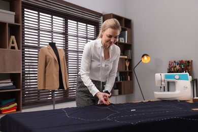 Dressmaker cutting fabric by following chalked sewing pattern in workshop