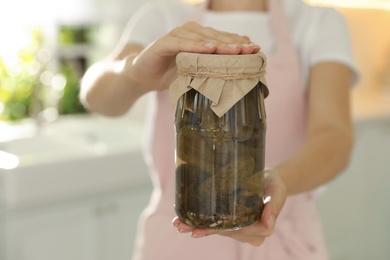 Woman holding jar of pickled cucumbers indoors, closeup
