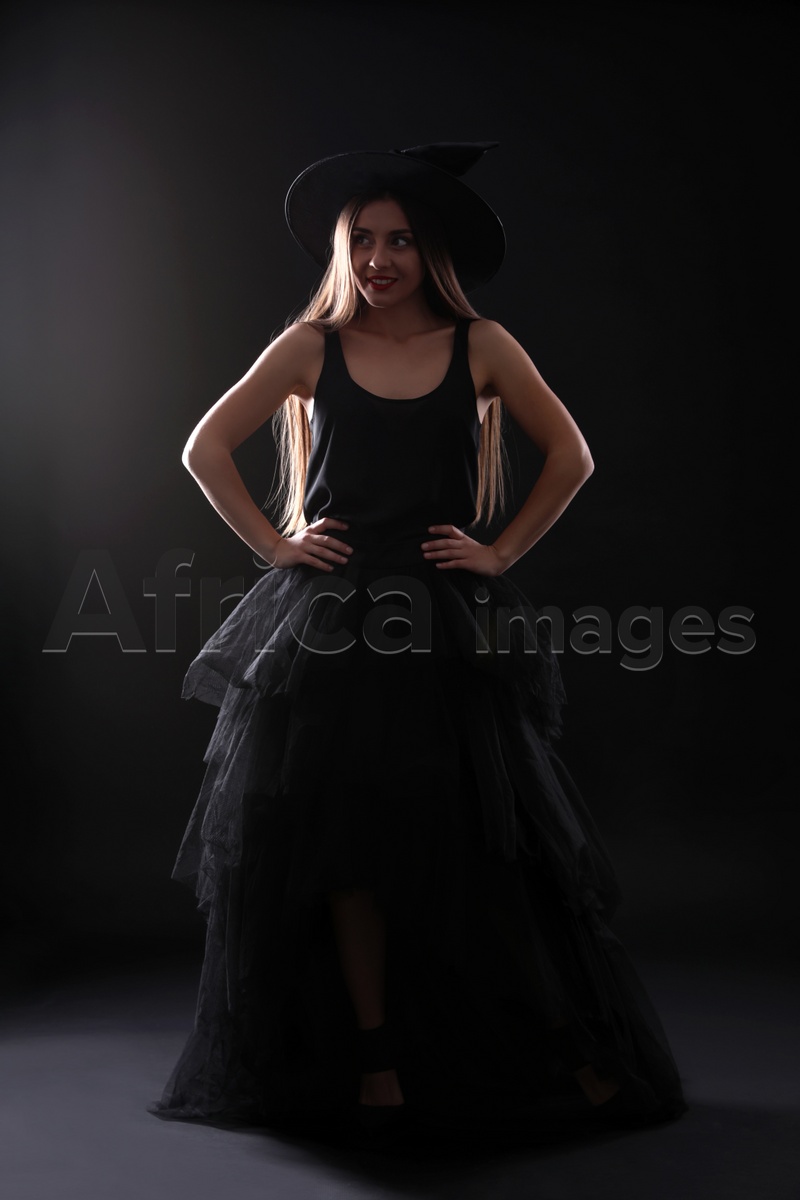 Young woman wearing witch costume on black background. Halloween party