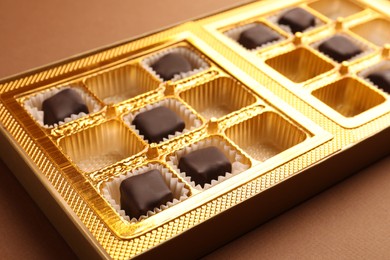 Photo of Partially empty box of chocolate candies on brown background, closeup