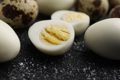 Photo of Peeled and unpeeled hard boiled quail eggs on black table, closeup
