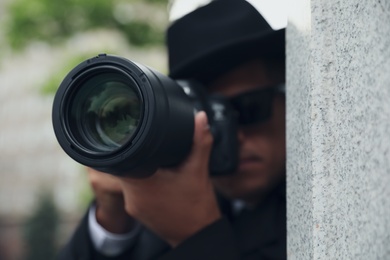 Private detective with modern camera spying outdoors, focus on lens
