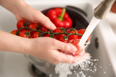 Woman washing fresh cherry tomatoes in kitchen sink, closeup