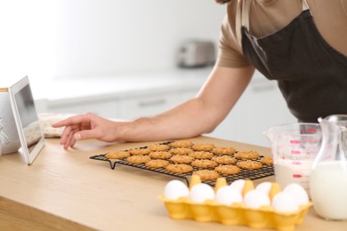 Photo of Man with freshly baked cookies watching online cooking course via tablet in kitchen, closeup