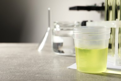 Container with urine sample for analysis and glassware on grey table, space for text