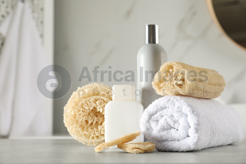 Natural loofah sponges, towel and cosmetic products on table in bathroom