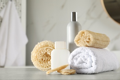 Photo of Natural loofah sponges, towel and cosmetic products on table in bathroom