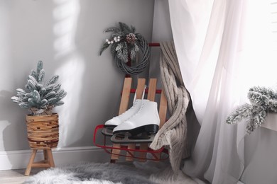 Pair of ice skates, sleigh and beautiful Christmas decor near window indoors