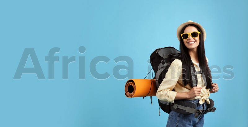 Happy female tourist with backpack on light blue background. Space for text