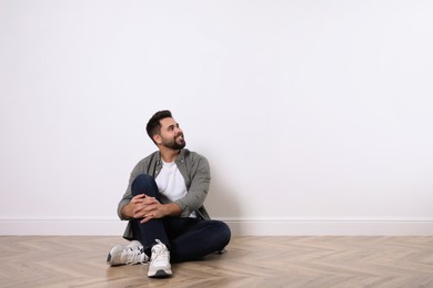 Young man sitting on floor near white wall indoors. Space for text