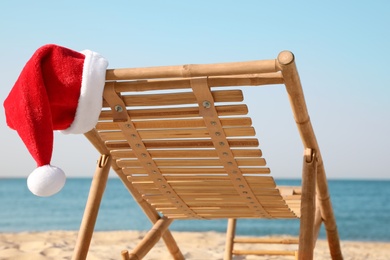 Photo of Sun lounger with Santa's hat on beach, closeup. Christmas vacation