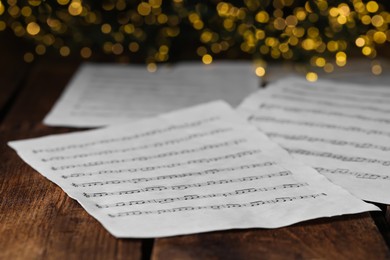 Photo of Closeup view of note sheets on wooden table against blurred lights. Christmas music