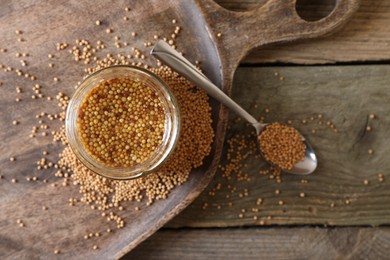 Photo of Jar and spoon of whole grain mustard on wooden table, flat lay. Space for text