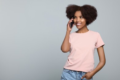 Photo of Smiling African American woman talking on smartphone against light grey background. Space for text