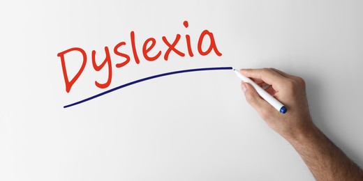 Image of Man writing word Dyslexia on white background, closeup. Banner design