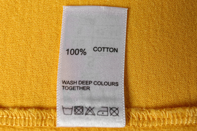 Clothing label with care symbols and material content on yellow shirt, top view