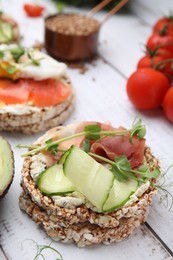 Photo of Crunchy buckwheat cakes with cream cheese, prosciutto and cucumber slice on white wooden table, closeup