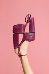 Photo of Woman wearing high heeled shoe with platform and square toes holding another one on pink background, closeup. Stylish presentation