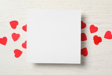 Blank card and red hearts on white wooden background, flat lay with space for text. Valentine's Day celebration