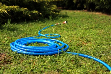 Photo of Blue watering hose on green grass outdoors, space for text