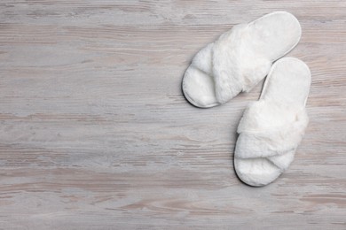 Pair of soft slippers on white wooden floor, top view. Space for text