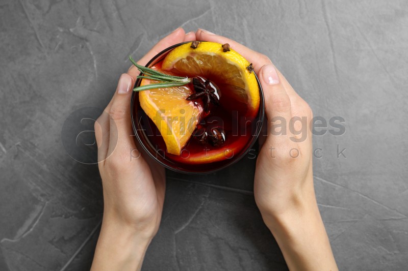 Young woman holding glass with tasty mulled wine at grey table, top view