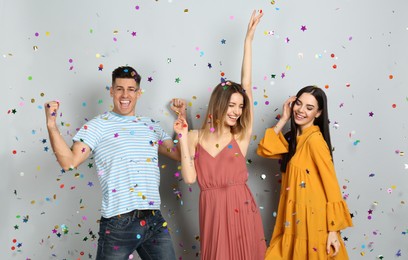 Happy friends and falling confetti on light grey background