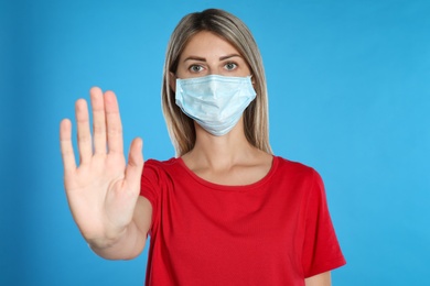 Woman in protective mask showing stop gesture on light blue background. Prevent spreading of coronavirus
