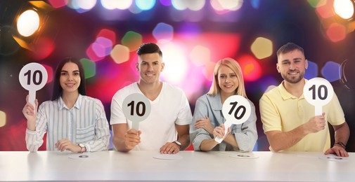 Panel of judges holding signs with highest score at table against blurred background. Bokeh effect