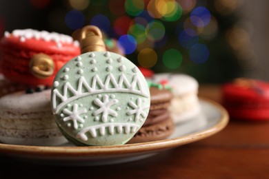 Beautifully decorated Christmas macarons on wooden table against blurred festive lights, closeup. Space for text