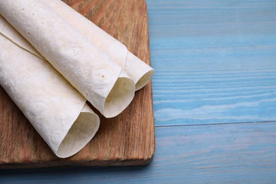 Photo of Delicious rolled Armenian lavash on light blue wooden table, space for text