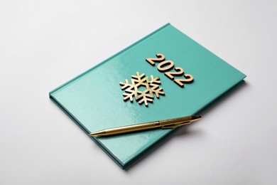 Turquoise planner, pen, wooden numbers and snowflake on white background. 2022 New Year aims