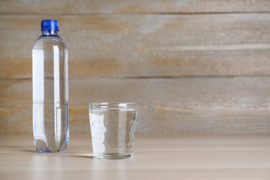 Glass and plastic bottle with water on table against wooden background, space for text