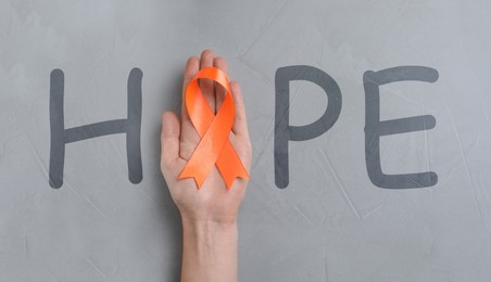 Word HOPE and woman with orange awareness ribbon on light grey background, top view  