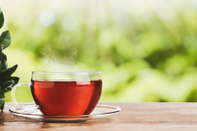 Glass cup of fresh hot tea on wooden table against blurred green background. Space for text