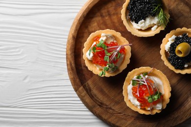 Photo of Delicious tartlets with red and black caviar served on white wooden table, top view. Space for text