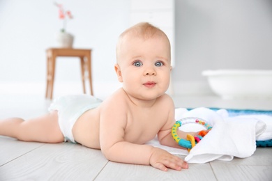 Photo of Cute little baby with rattle on floor in bathroom