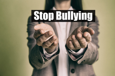 Young woman showing sign STOP BULLYING on color background, closeup 
