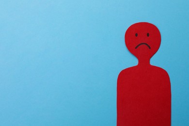 Photo of Red paper cutout of person with sad face on light blue background, space for text. Stress management