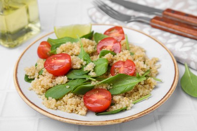 Photo of Delicious quinoa salad with tomatoes and spinach leaves served on white tiled table, closeup