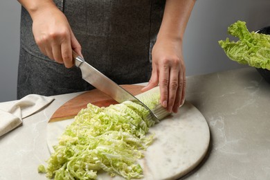 Photo of Woman cutting fresh Chinese cabbage at light grey table, closeup