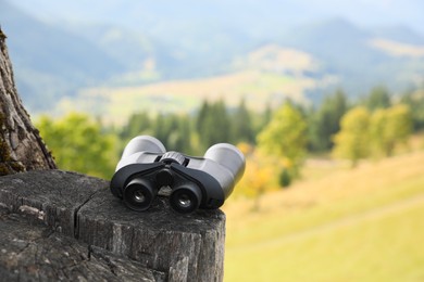 Modern binoculars on tree stump outdoors, space for text