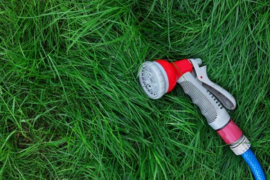 Watering hose with sprinkler on green grass outdoors, top view. Space for text