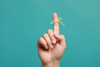 Photo of Man showing index finger with tied bow as reminder on turquoise background, closeup