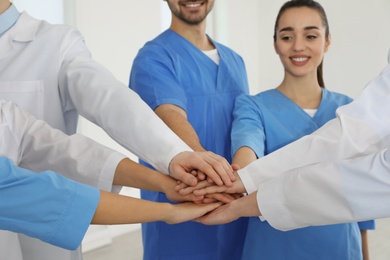 Team of medical workers holding hands together indoors. Unity concept
